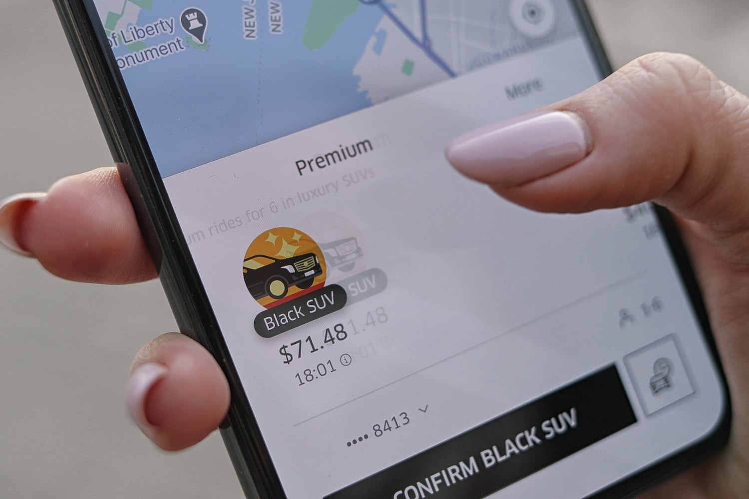 A person with only their hand visible using the Uber app to select a black SUV